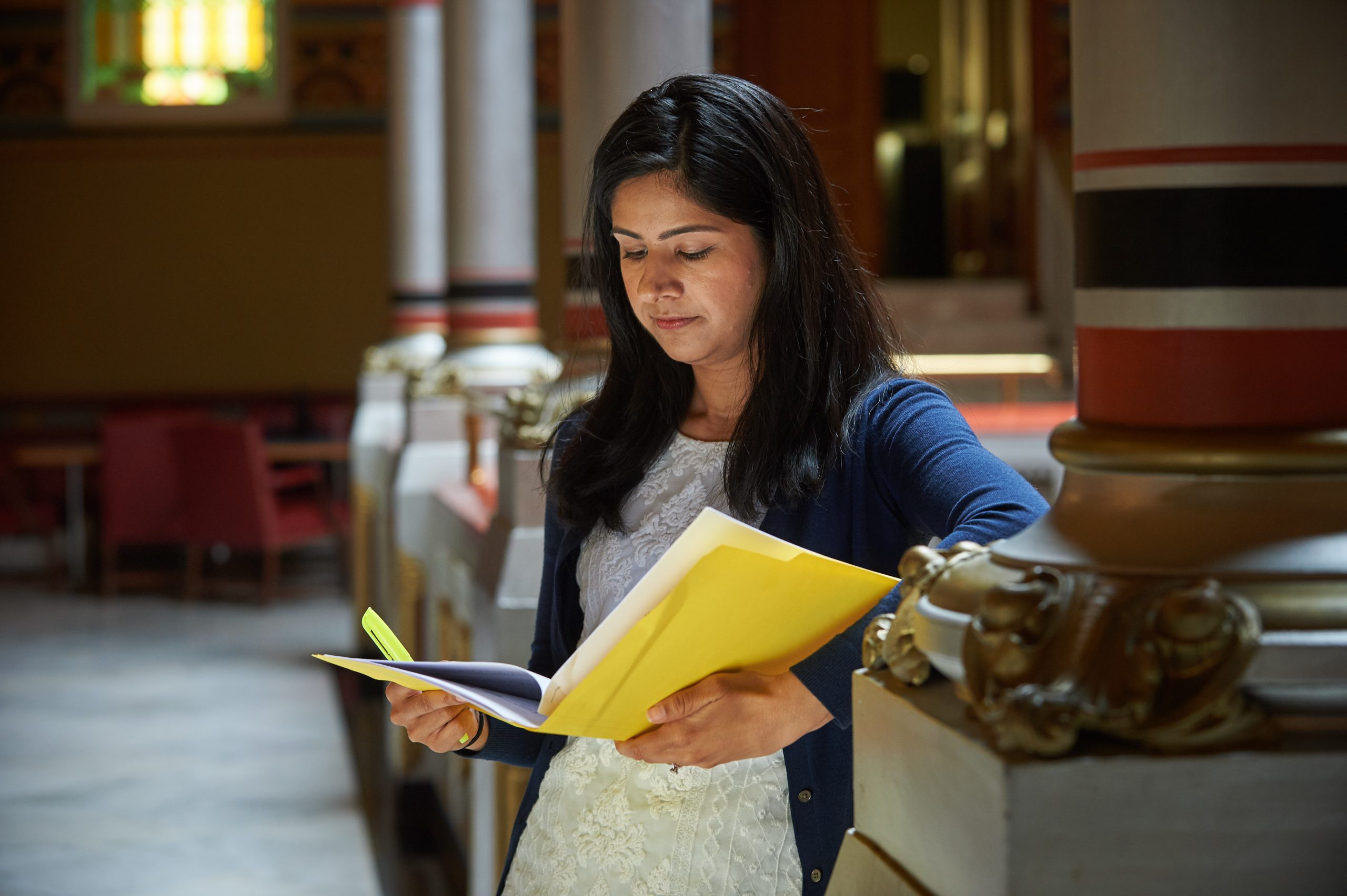 Student reviewing notes inside a historic academic building with classical columns and ornate decor.